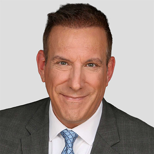 Professional headshot of a smiling man in a gray suit and blue tie against a light gray background.